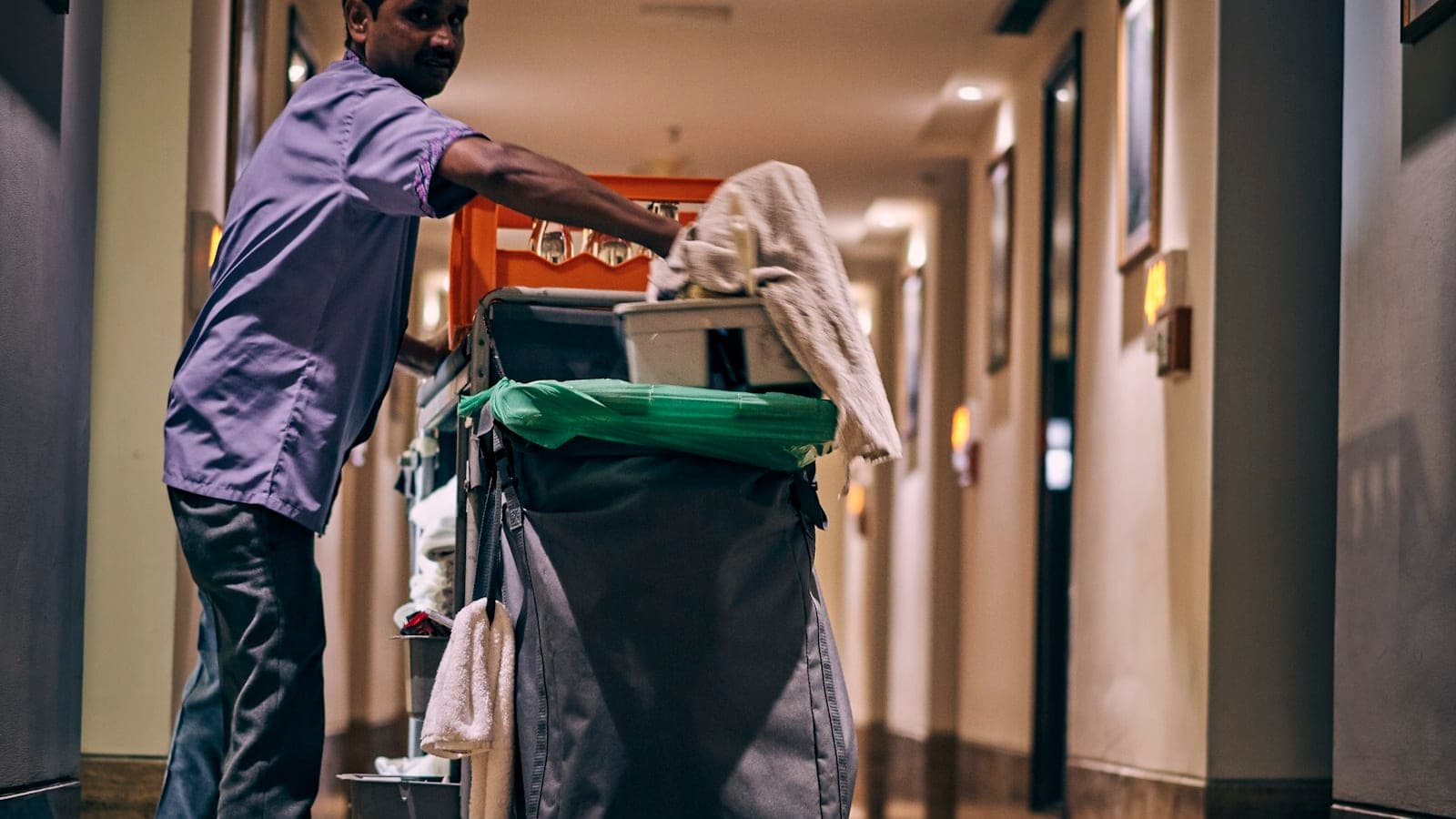 Cleaner pushing a cleaning trolley along a corridor