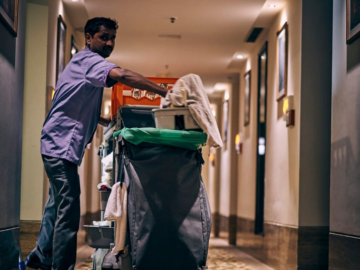 Cleaner pushing a cleaning trolley along a corridor