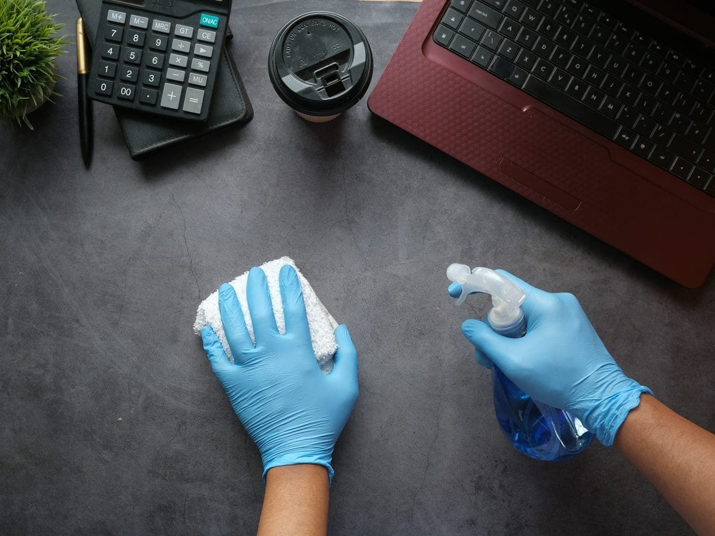 Cleaner wearing blue gloves wiping a desk next to a laptop