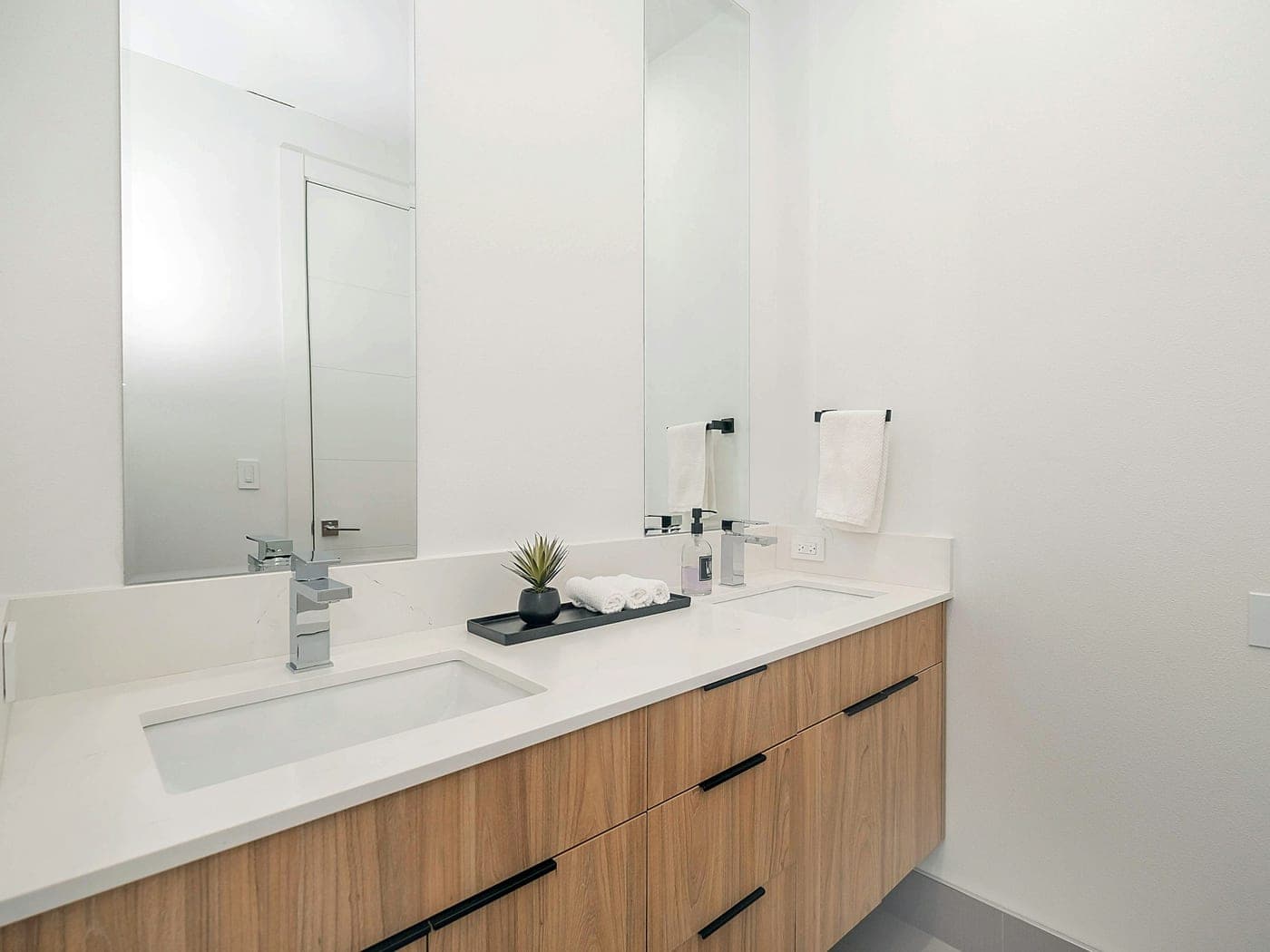 White washroom with a double basin, mirror and wooden cabinet