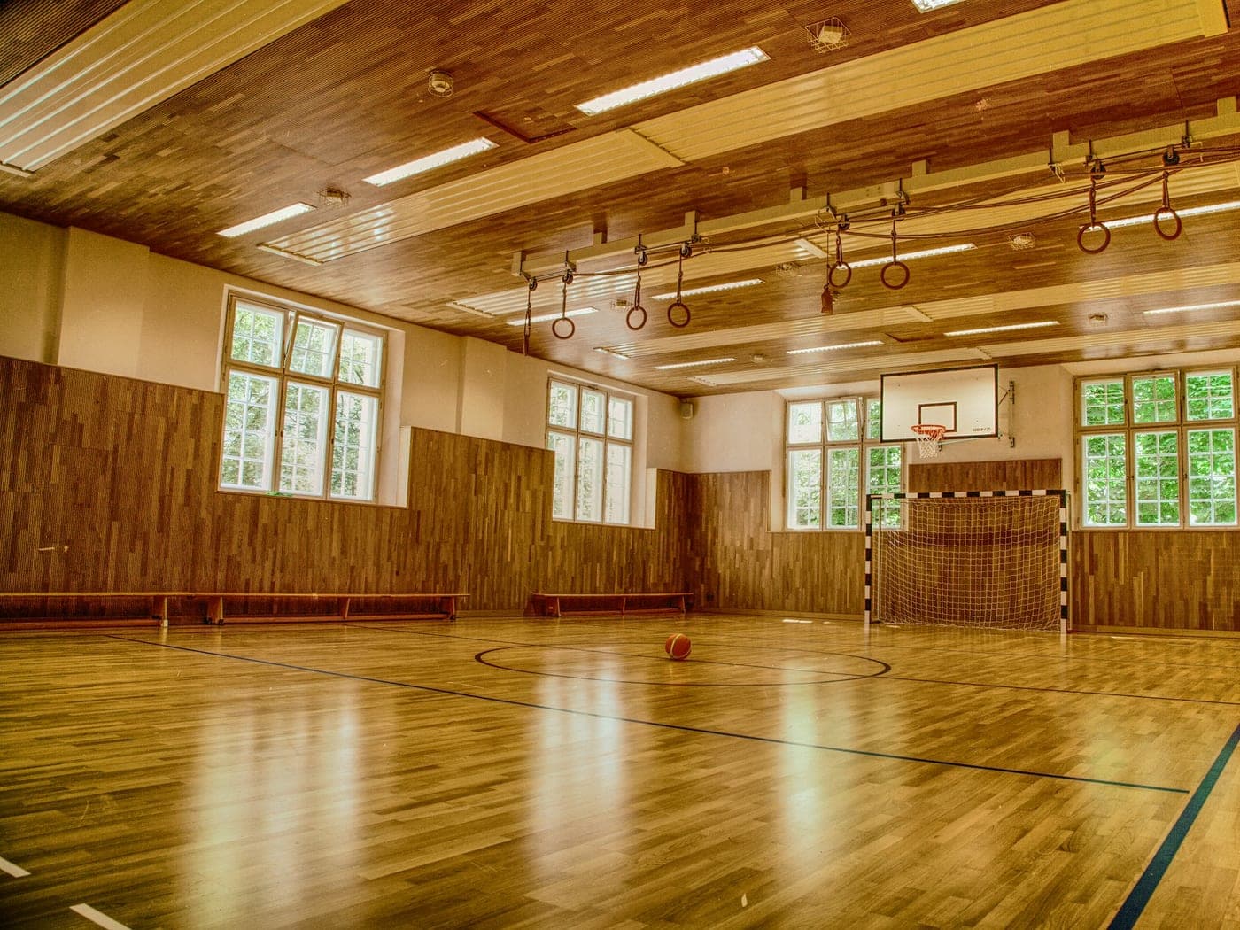 Sports hall with a wooden floor, basketball backboard and daylight through the windows