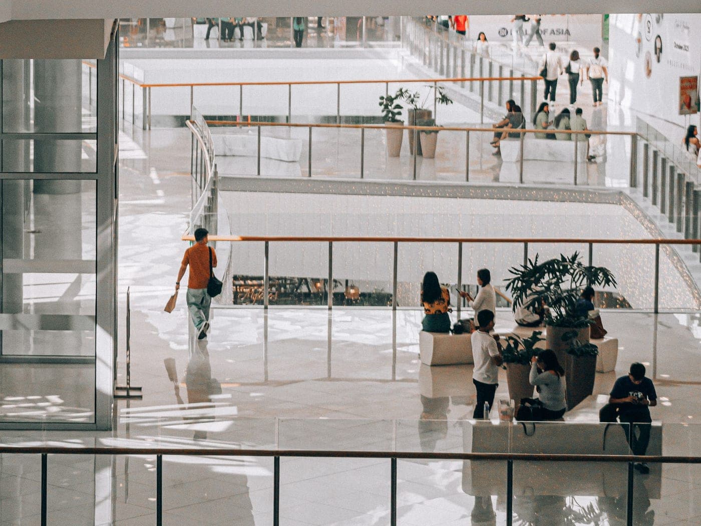 Bright shopping centre with glass balustrades, plants and visitors