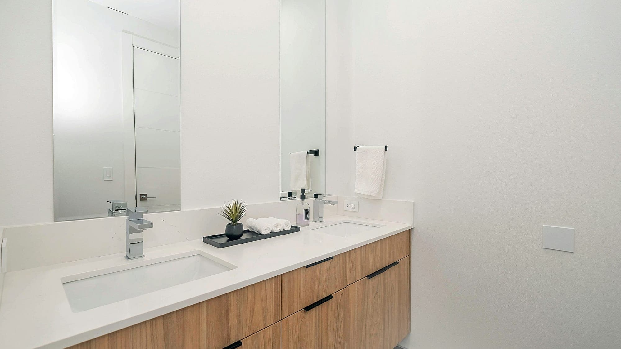 White washroom with a double basin, mirror and wooden cabinet