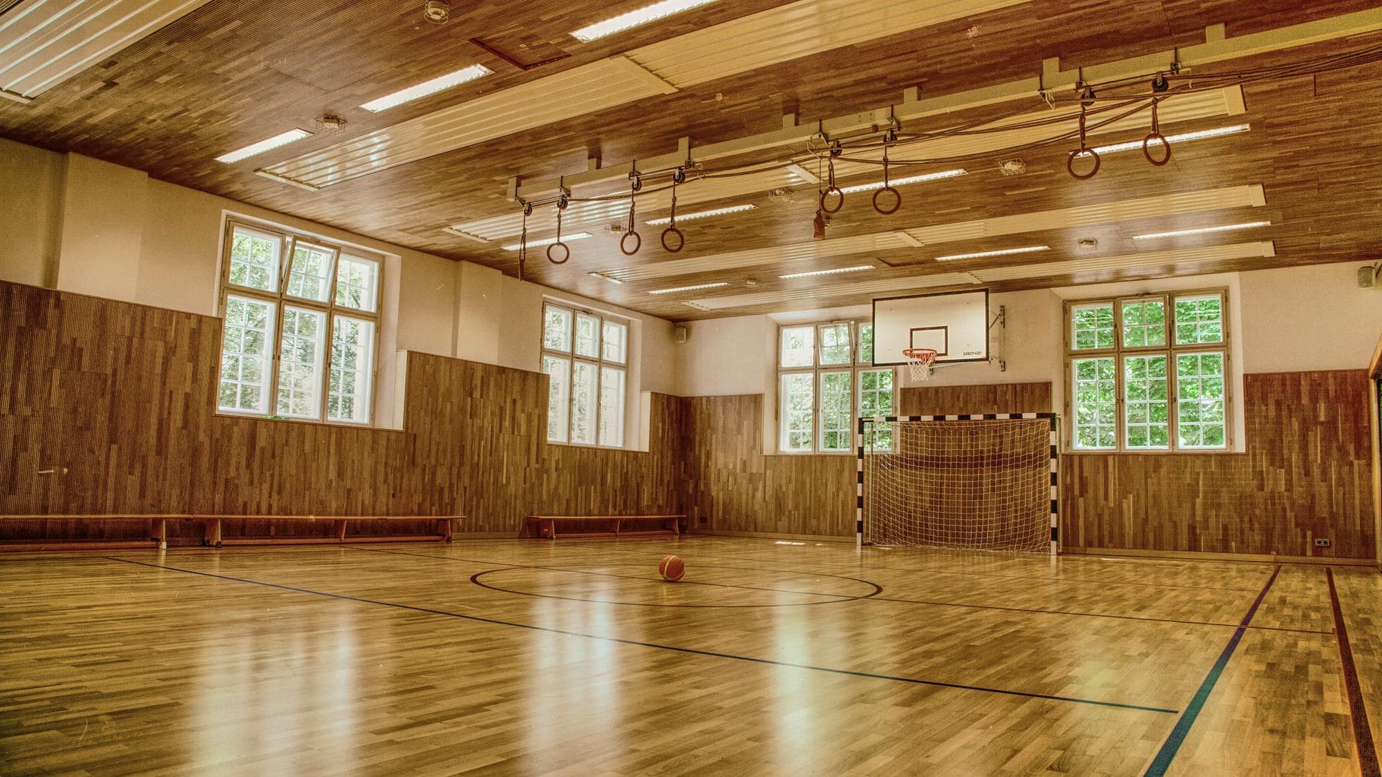 Sports hall with a wooden floor, basketball backboard and daylight through the windows