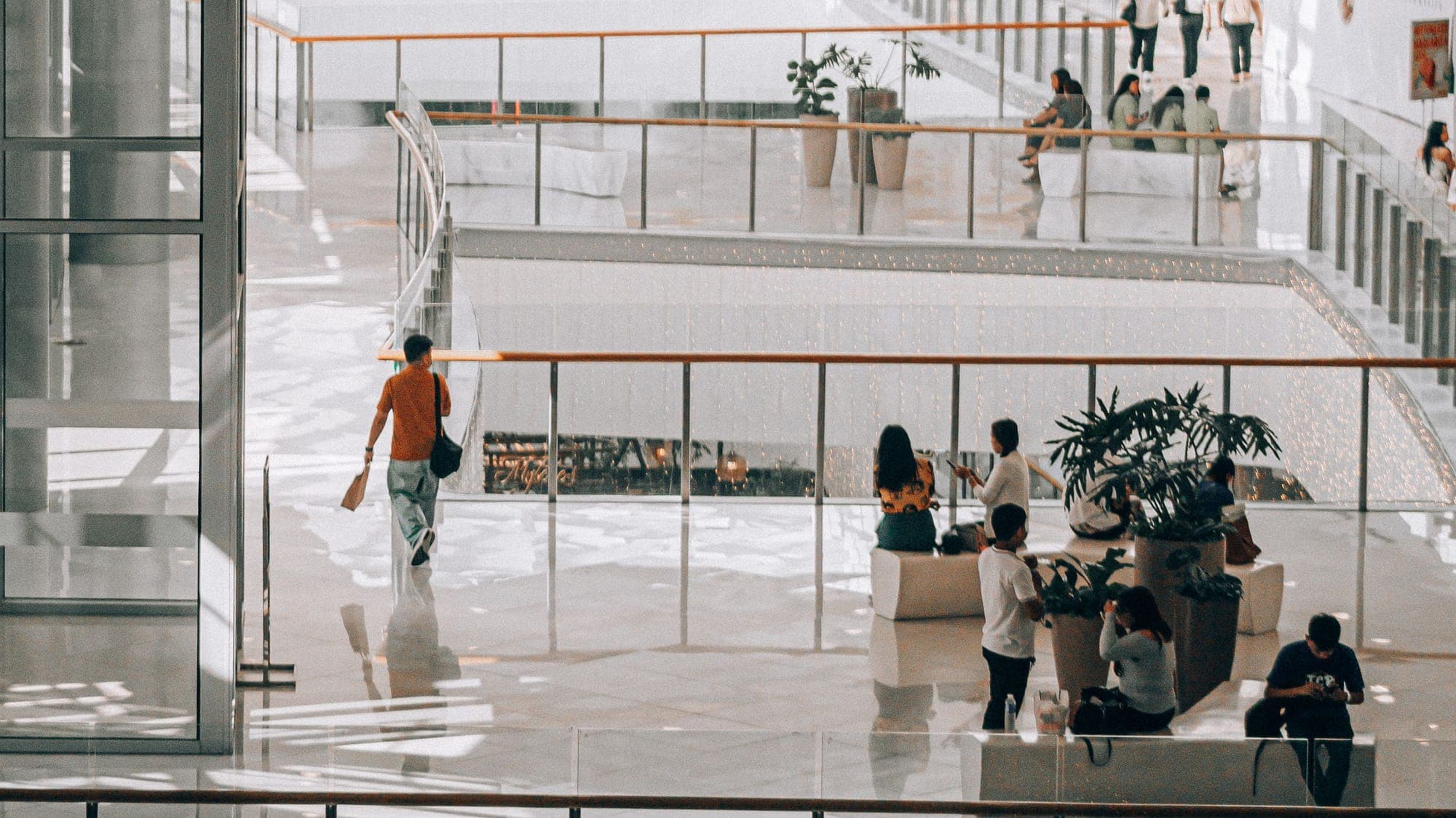 Bright shopping centre with glass balustrades, plants and visitors