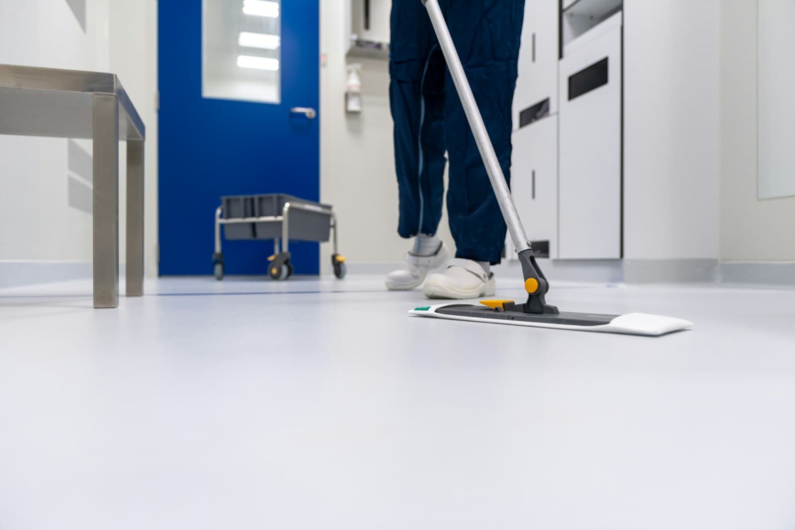 Cleaner in workwear running a flat mop over a light floor
